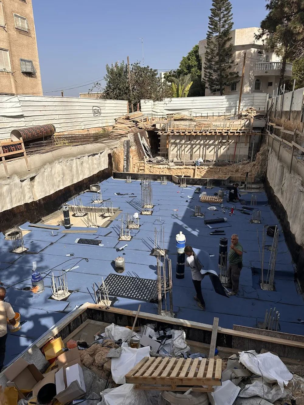 קומת מרתף בשלב איטום עם יריעות כחולות וזיני ברזל של עמודים