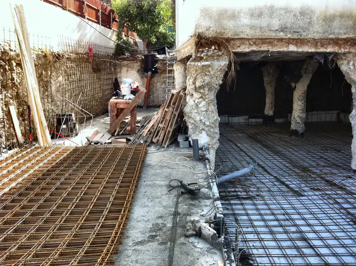 רשתות זיון פרוסות על הרצפה לפני היציקה, לצד עמודים יצוקים